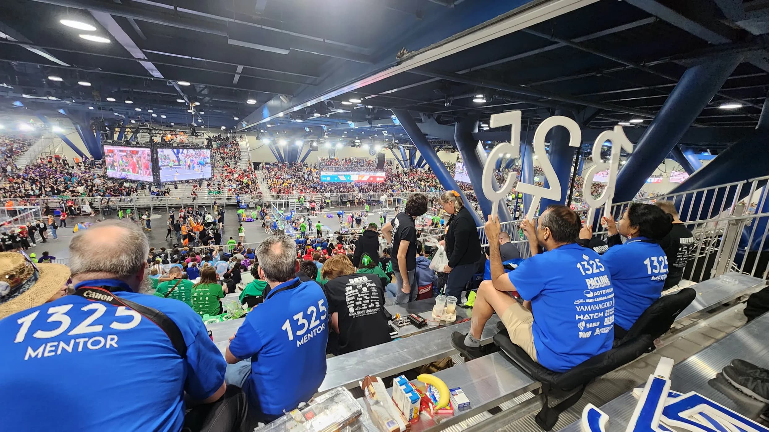 The stands at a FIRST Robotics championship, team 1325 mentors in the foreground and the competition fields below