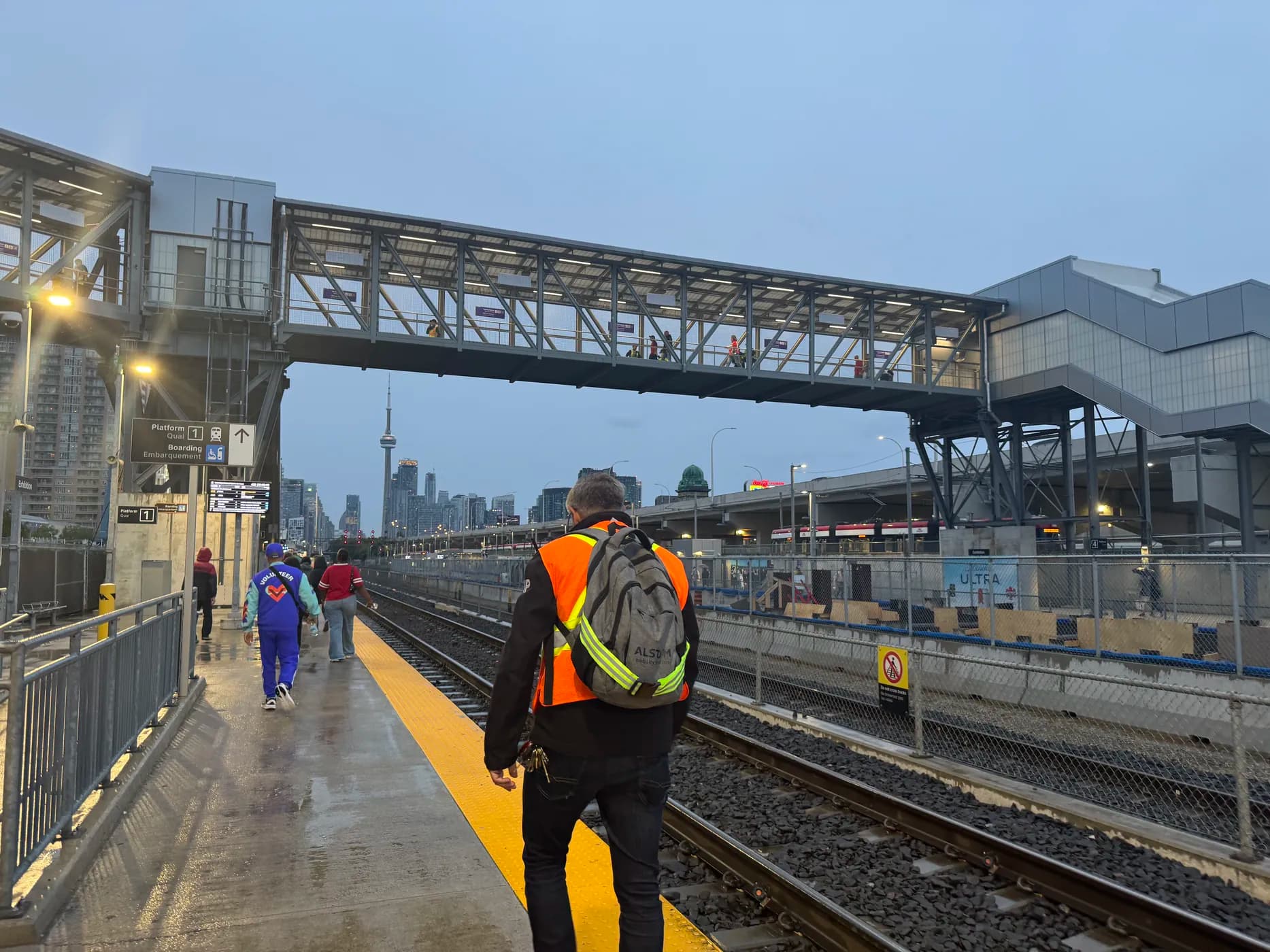 A wet GO Transit platform at dusk with the CN Tower in the distance