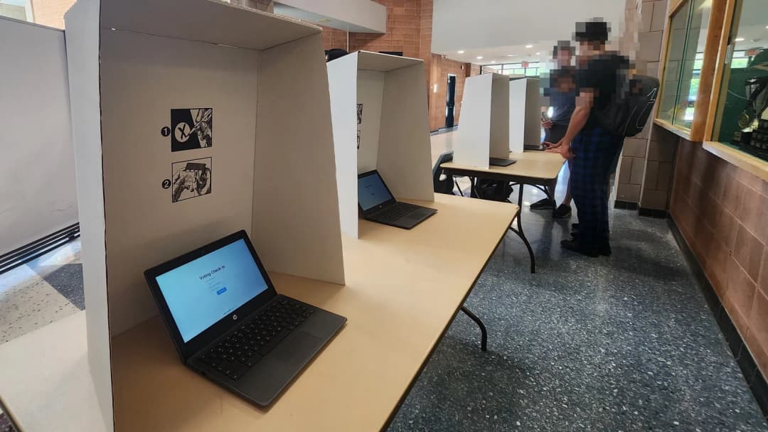 Cardboard voting booths with Chromebooks set up in a school hallway on election day